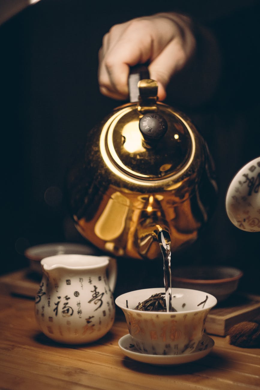 person holding gold teapot pouring white ceramic teacup