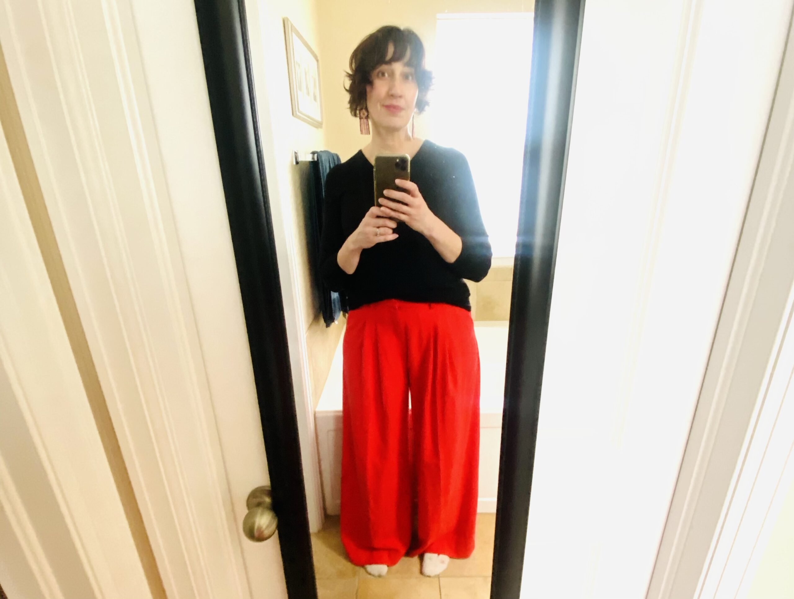 Woman in red pants and black sweater looking in hanging mirror